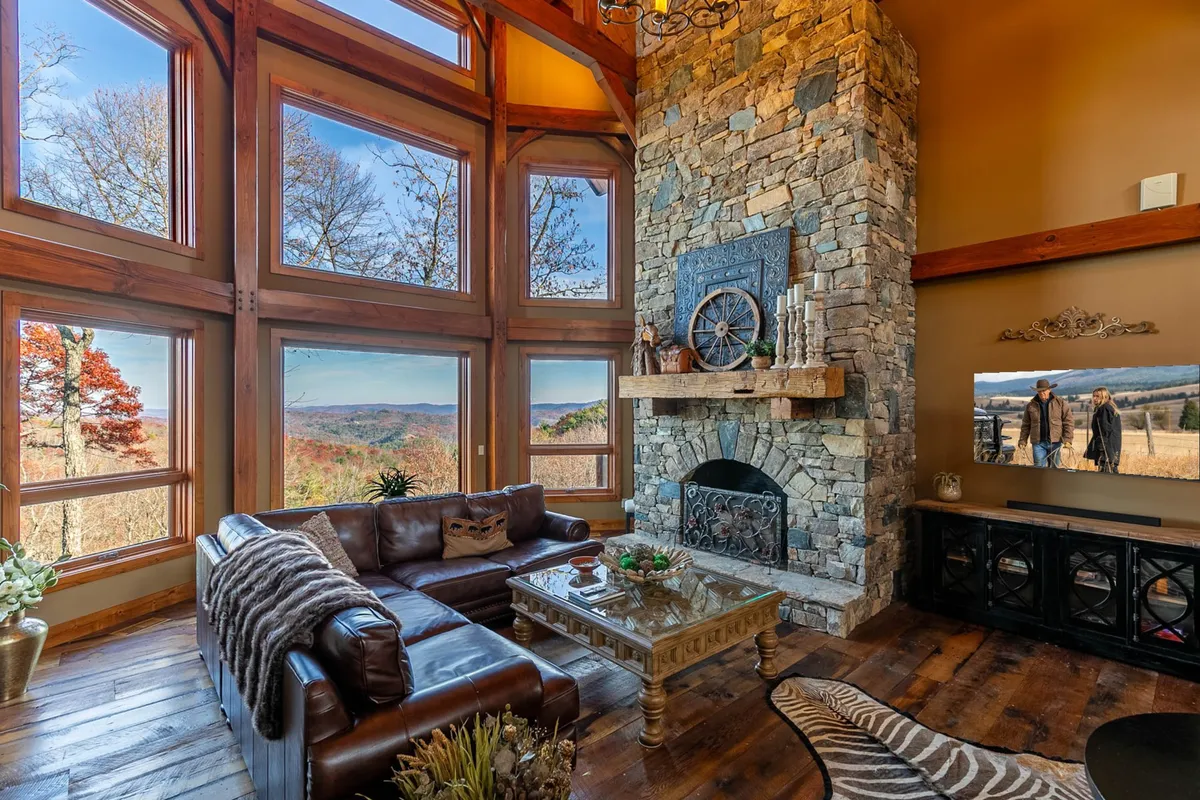 The spacious interior living room showcases a large stone fireplace and expansive windows that frame the natural beauty outside. A leather sofa and wooden coffee table create a cozy atmosphere ideal for relaxation and socializing after a day of exploring.