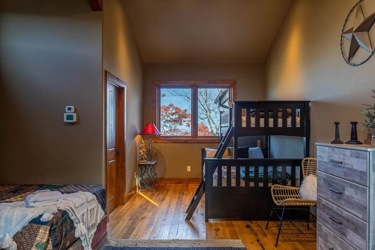 A warm, inviting bunkroom with a bunk bed, a window looking out to the natural surroundings, and a red lamp, designed for relaxed play and quiet time. This space is perfect for children or teens to enjoy their own adventures.
