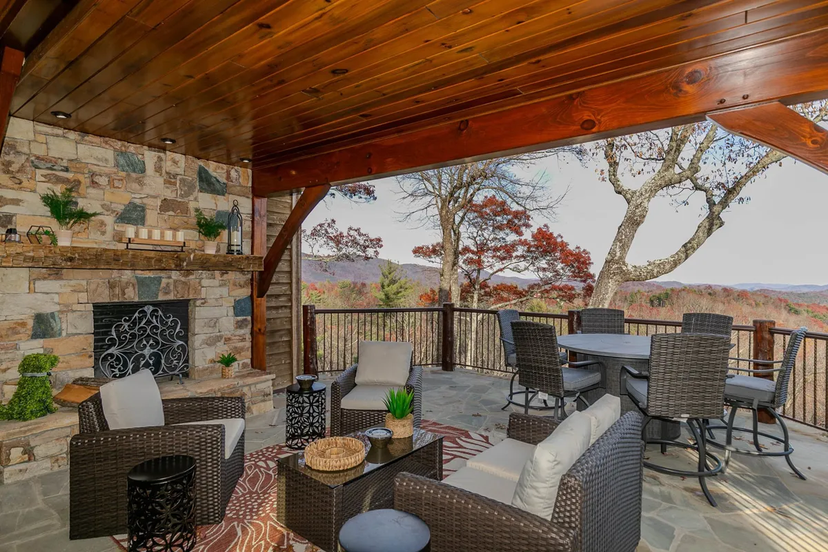 A cozy exterior area featuring a stone fireplace, wicker furniture, and a scenic view of the mountains beyond. The arrangement invites intimate gatherings, relaxation, and enjoying sunsets in serene privacy.