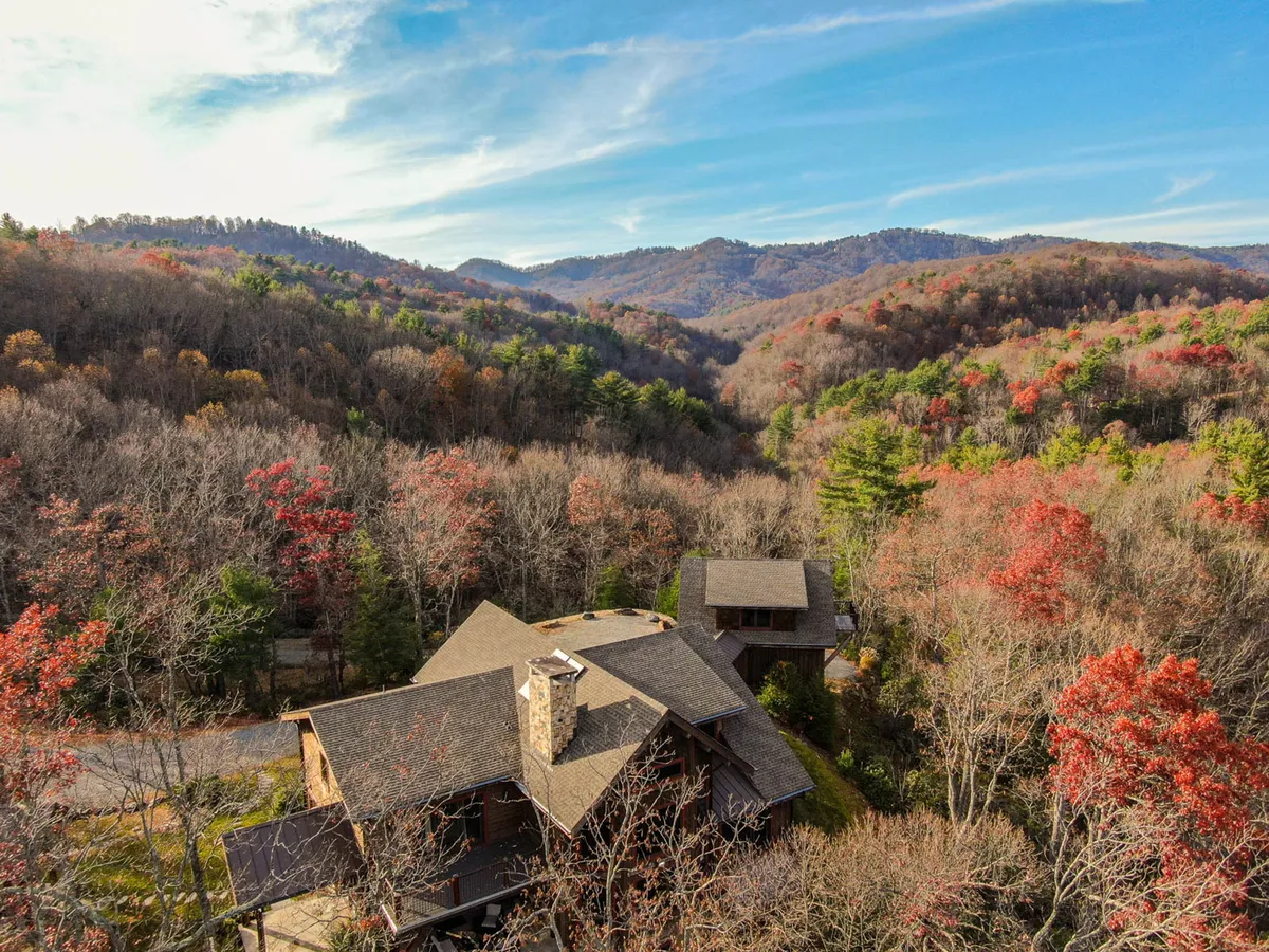 A view of the house nestled in a lush valley, surrounded by vibrant, colorful trees and distant Blue Ridge mountains. The setting exudes tranquility, privacy, and showcases expansive natural beauty with no neighbors in sight.
