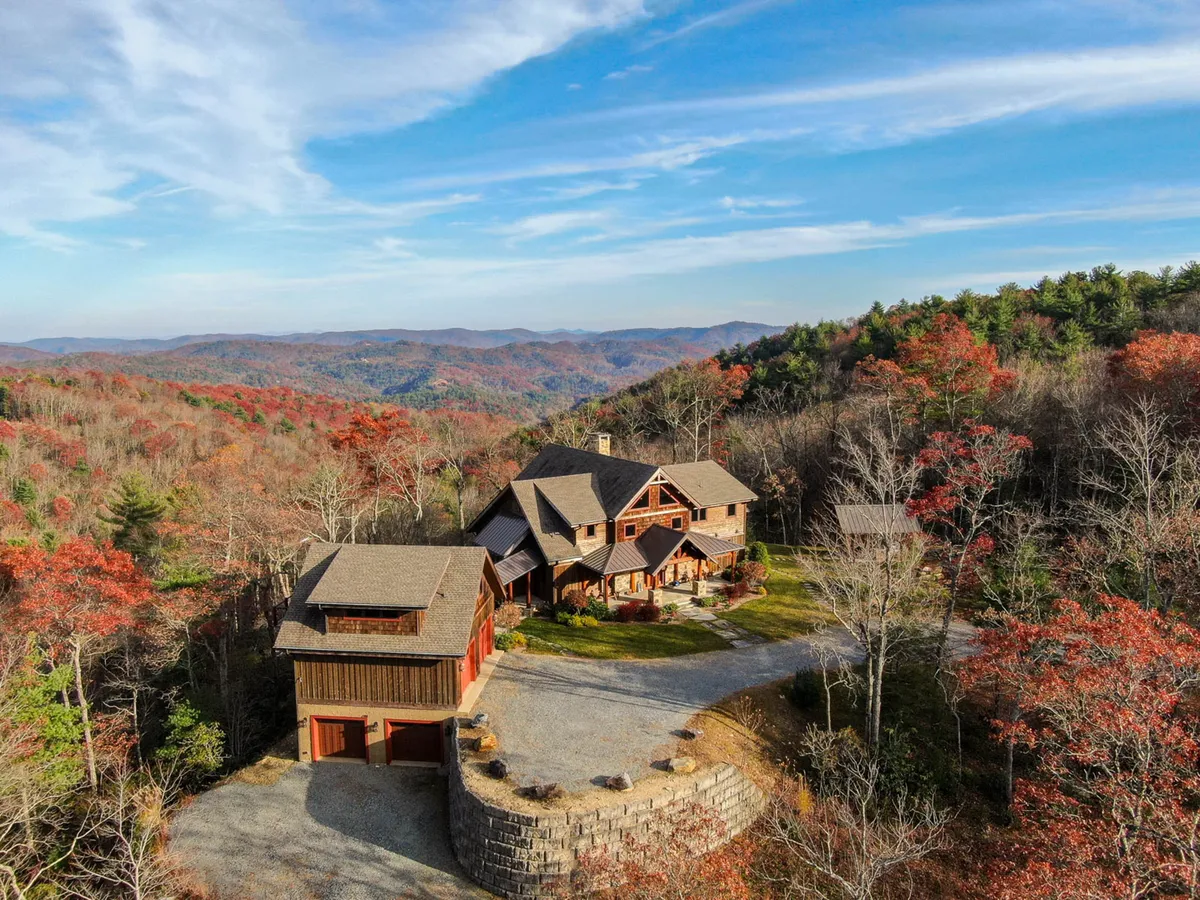 The hero image showcases the main house and an adjacent structure set against a sweeping backdrop of the Blue Ridge Mountains. The expansive property features lush greenery and open spaces, inviting guests to embrace outdoor living. The serene natural surroundings emphasize tranquility, while hints of an outdoor kitchen and fire pit suggest spaces for gathering and relaxation.