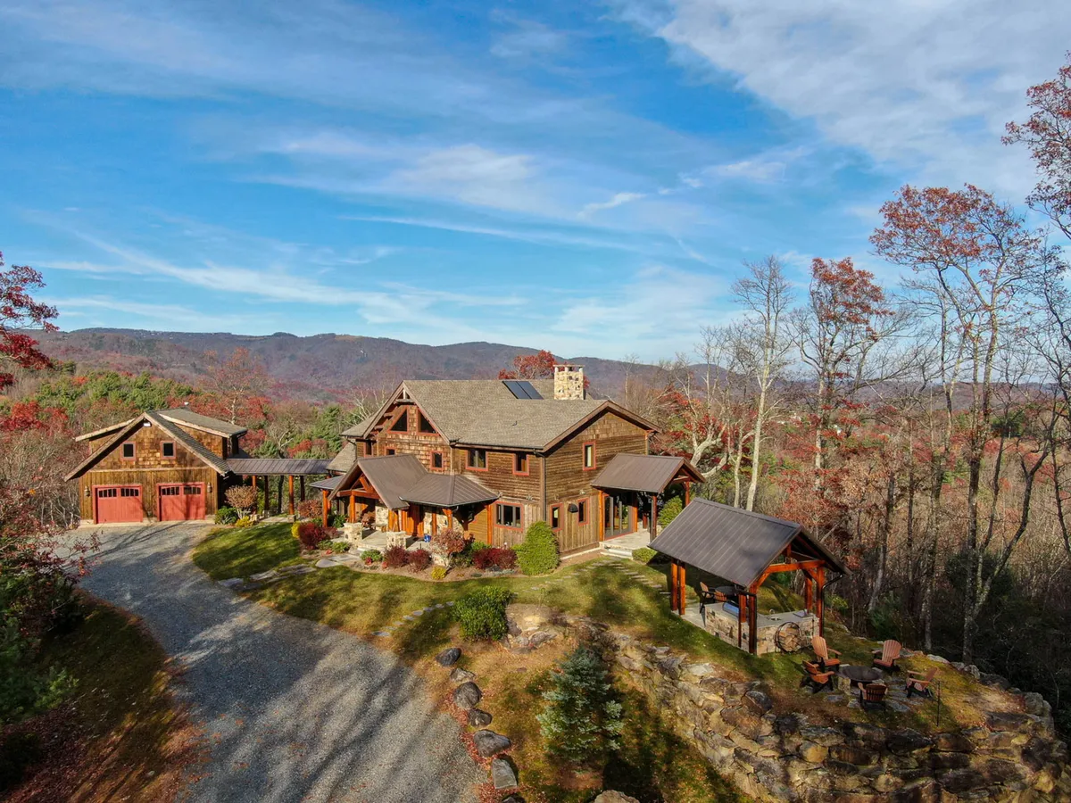 This image captures the main house and garage surrounded by a scenic mountain backdrop, with a stone pathway and inviting outdoor seating area. The setting is perfect for family gatherings, outdoor barbecues, and relaxing in nature, reinforcing the expansive, welcoming feel of the property.
