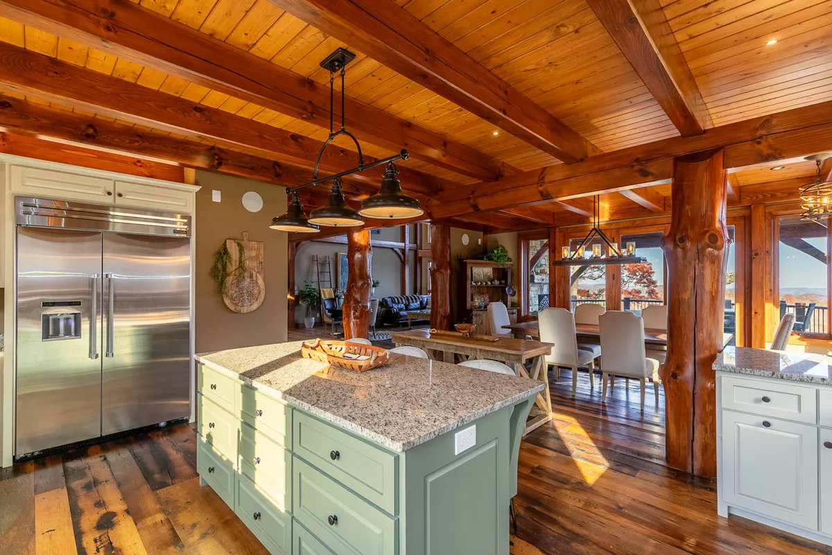 A modern, well-equipped kitchen with a granite island, wooden beams, stainless steel appliances (including Thermador), and an adjacent dining area. The space is bright, spacious, and designed for effortless meal preparation and entertaining.